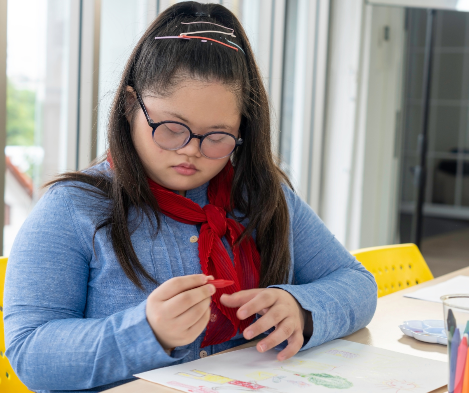 A young person drawing at a table, representing person-centered support and daily-life care routines.