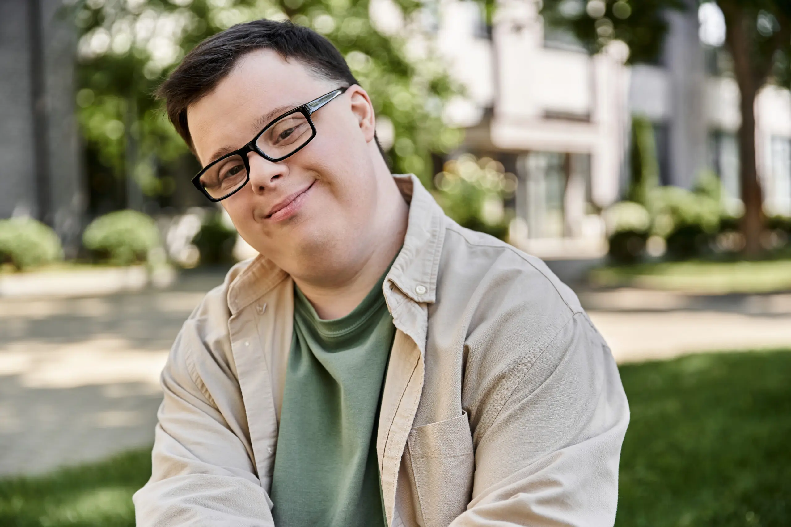 A young man with Down syndrome smiles in a park