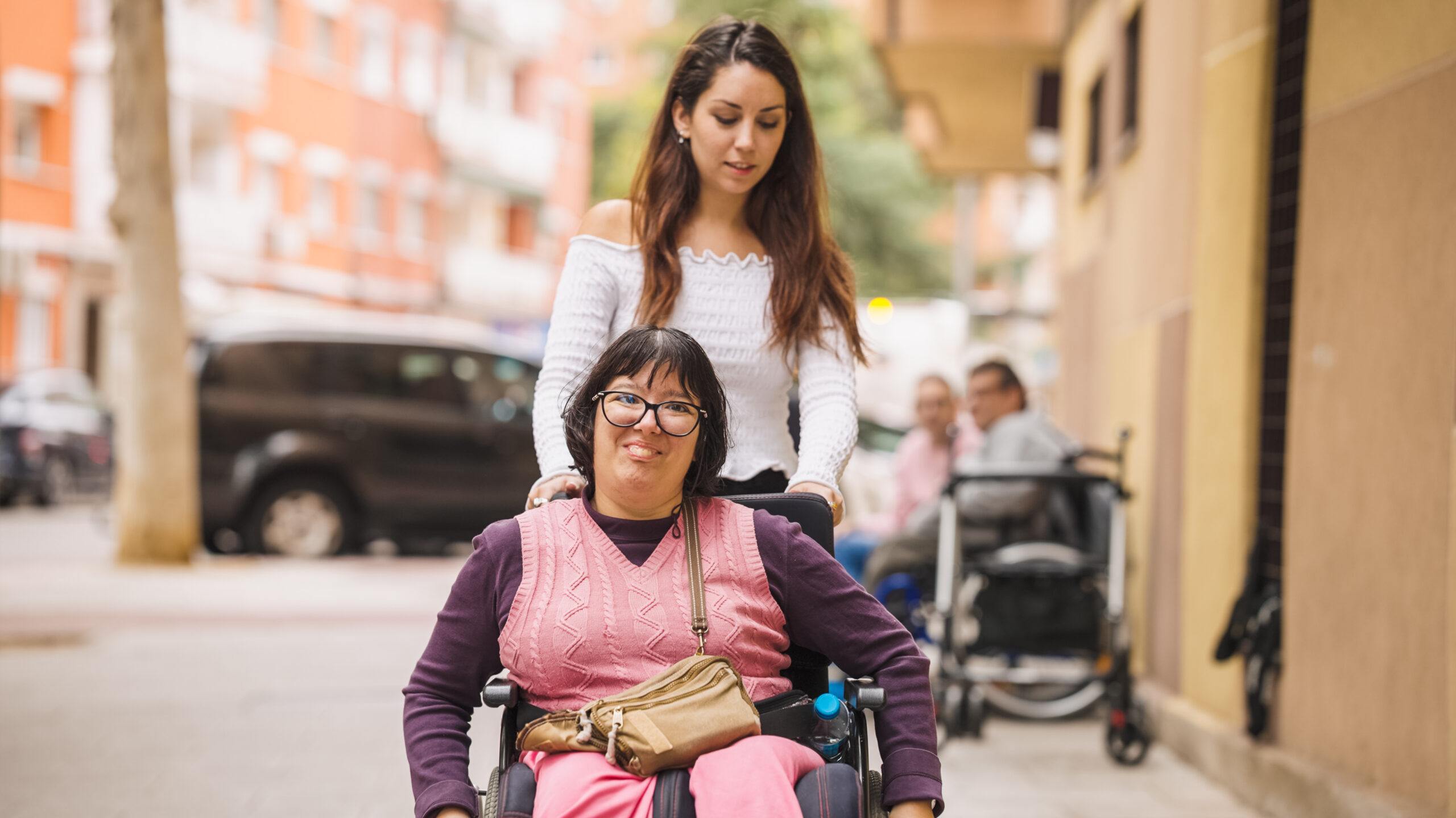 A support professional assisting a woman who uses a wheelchair outdoors