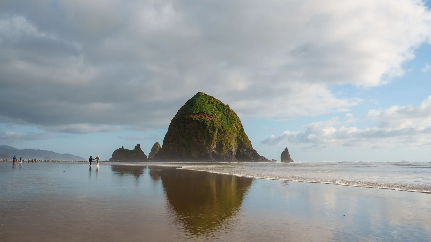 Haystack Rock at Cannon Beach on the Clatsop County coast, with two people walking along the wet sand